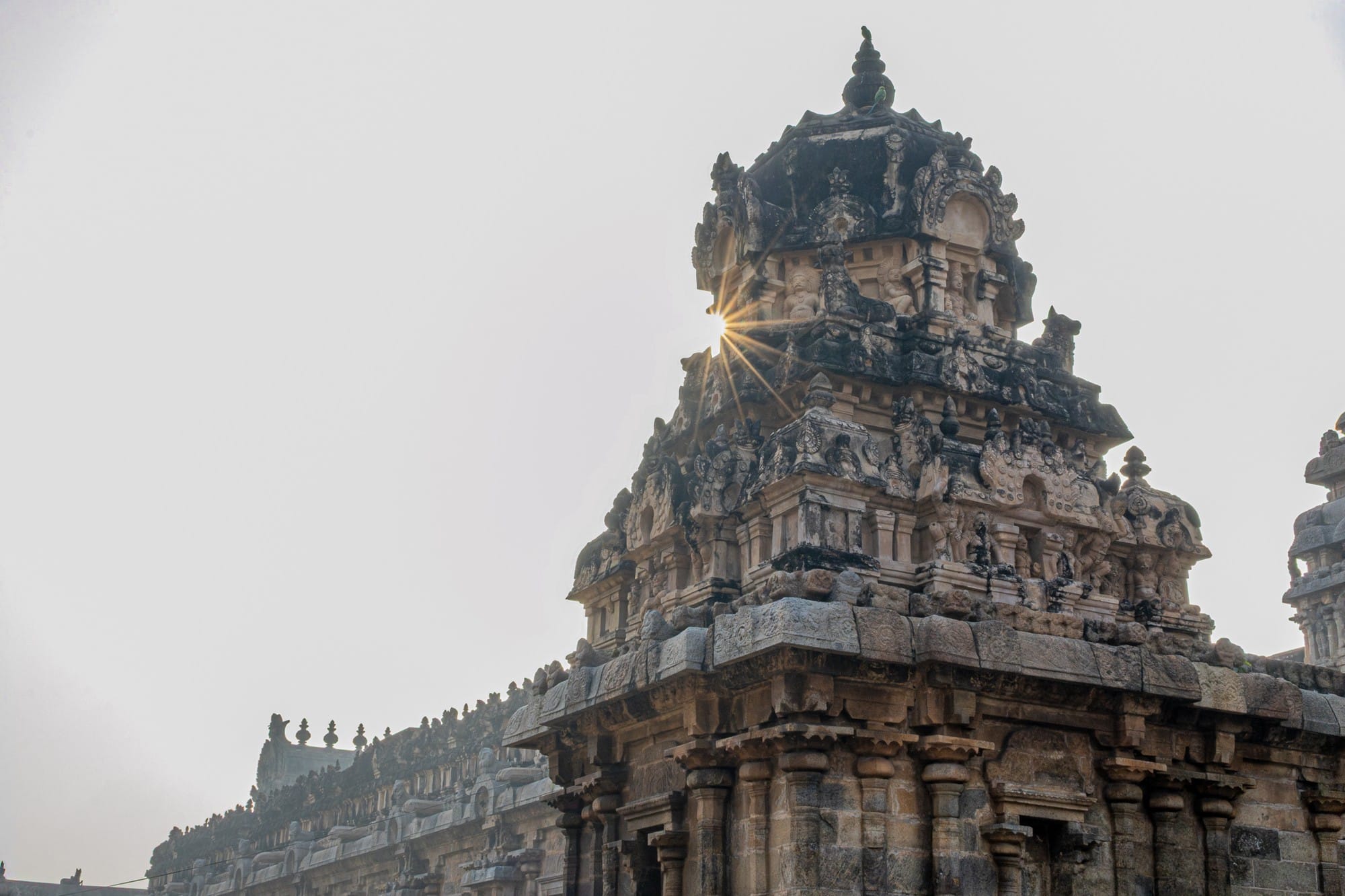 Carved stone temple tower with sunlight peeking through its facade.