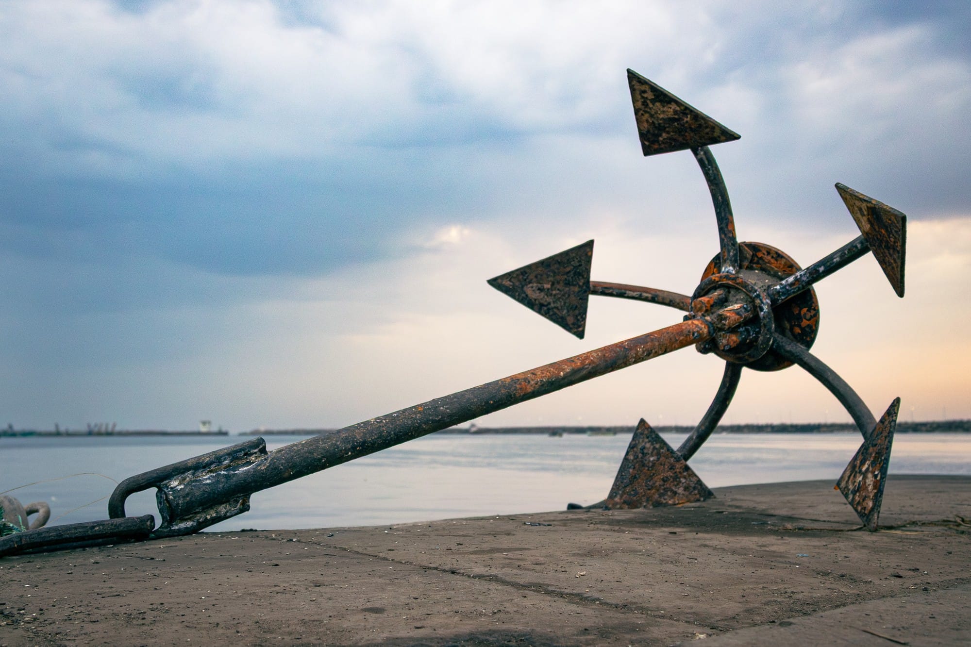 Metal arrow-shaped sculpture on a beach beneath a softly clouded sky.