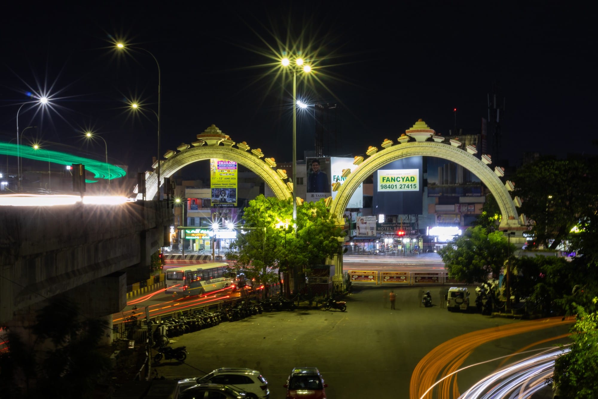 Illuminated ornamental gateways and traffic light trails at night.