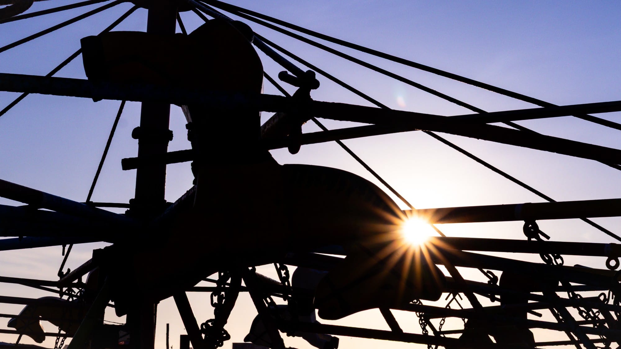 Silhouetted waterfront machinery and cables framing a low sun.