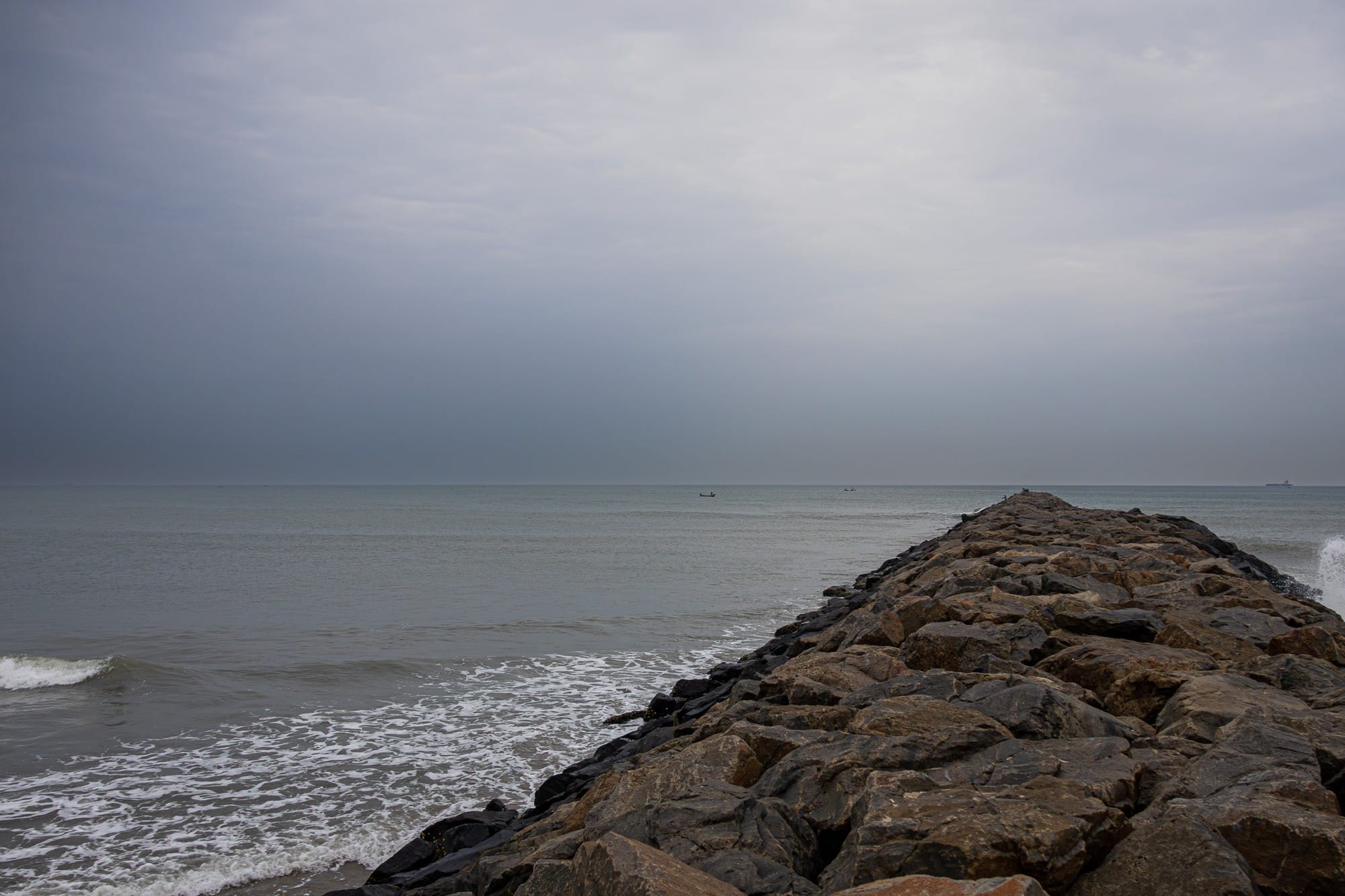 Rocky breakwater reaching into a calm sea beneath a grey sky.