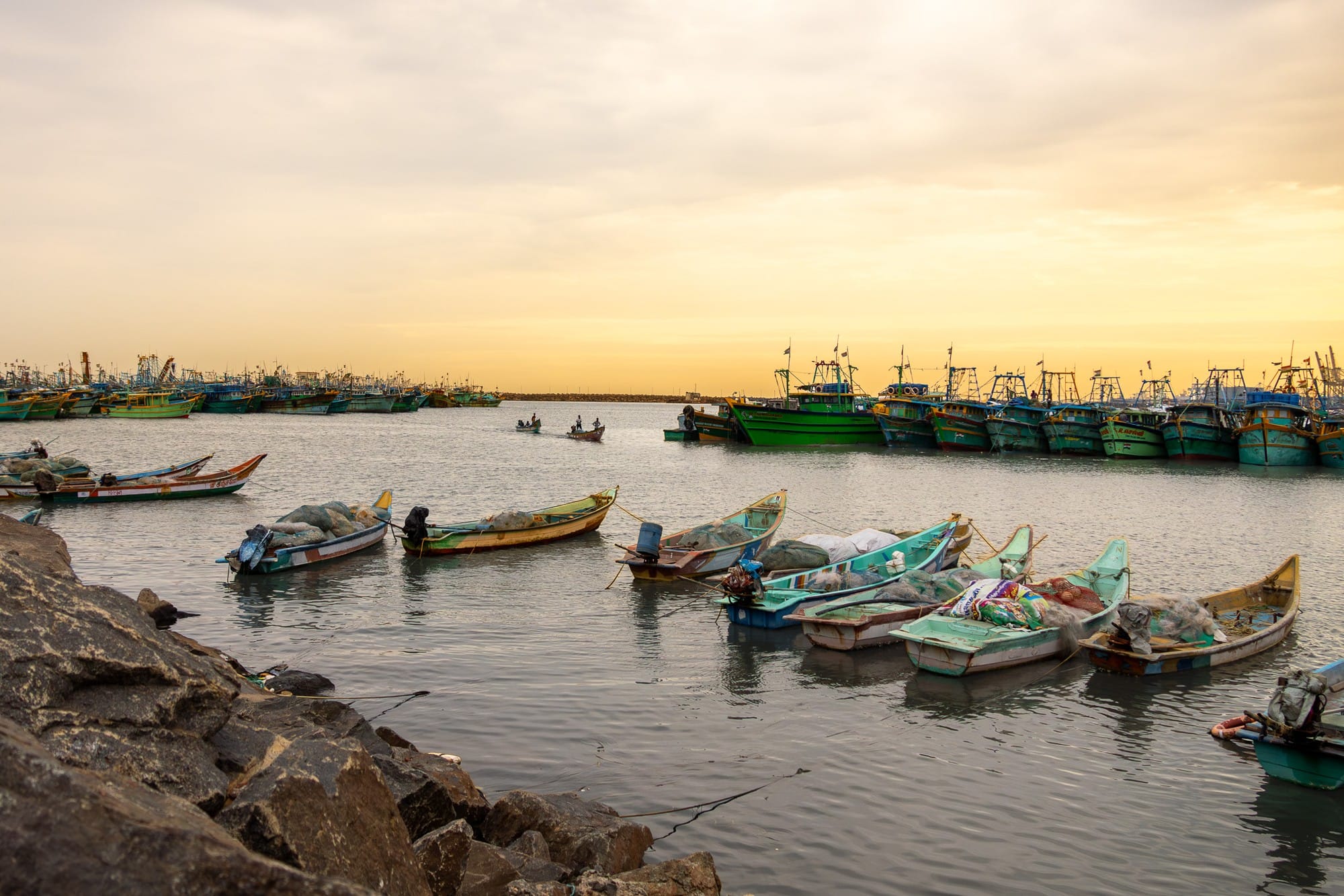 Fishing boats floating in a harbour under a warm clouded sky.