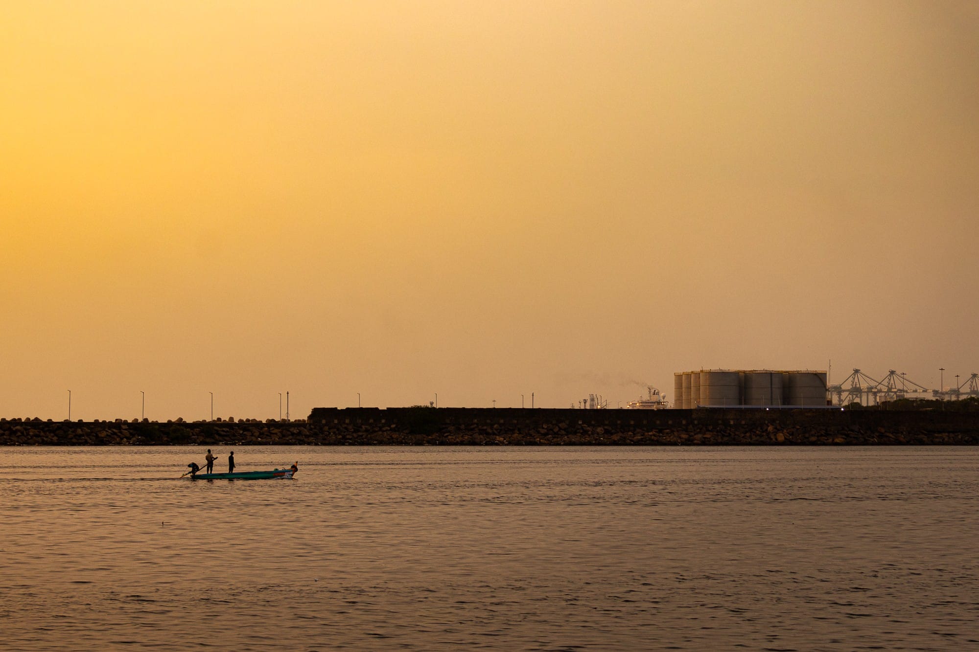 Distant figures and a small boat on water beneath a golden sky.