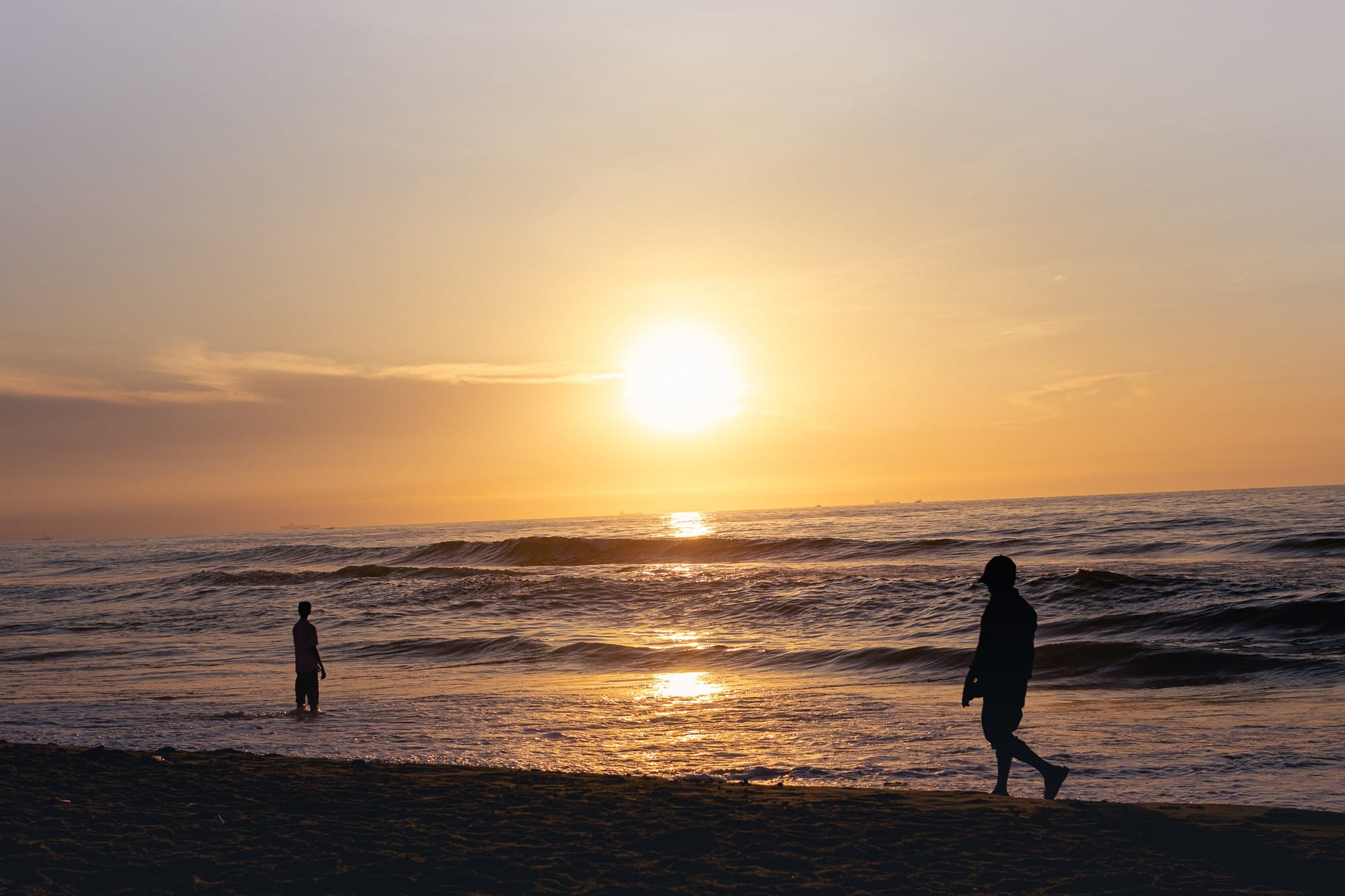 Golden sun above the ocean with people silhouetted along the shoreline.