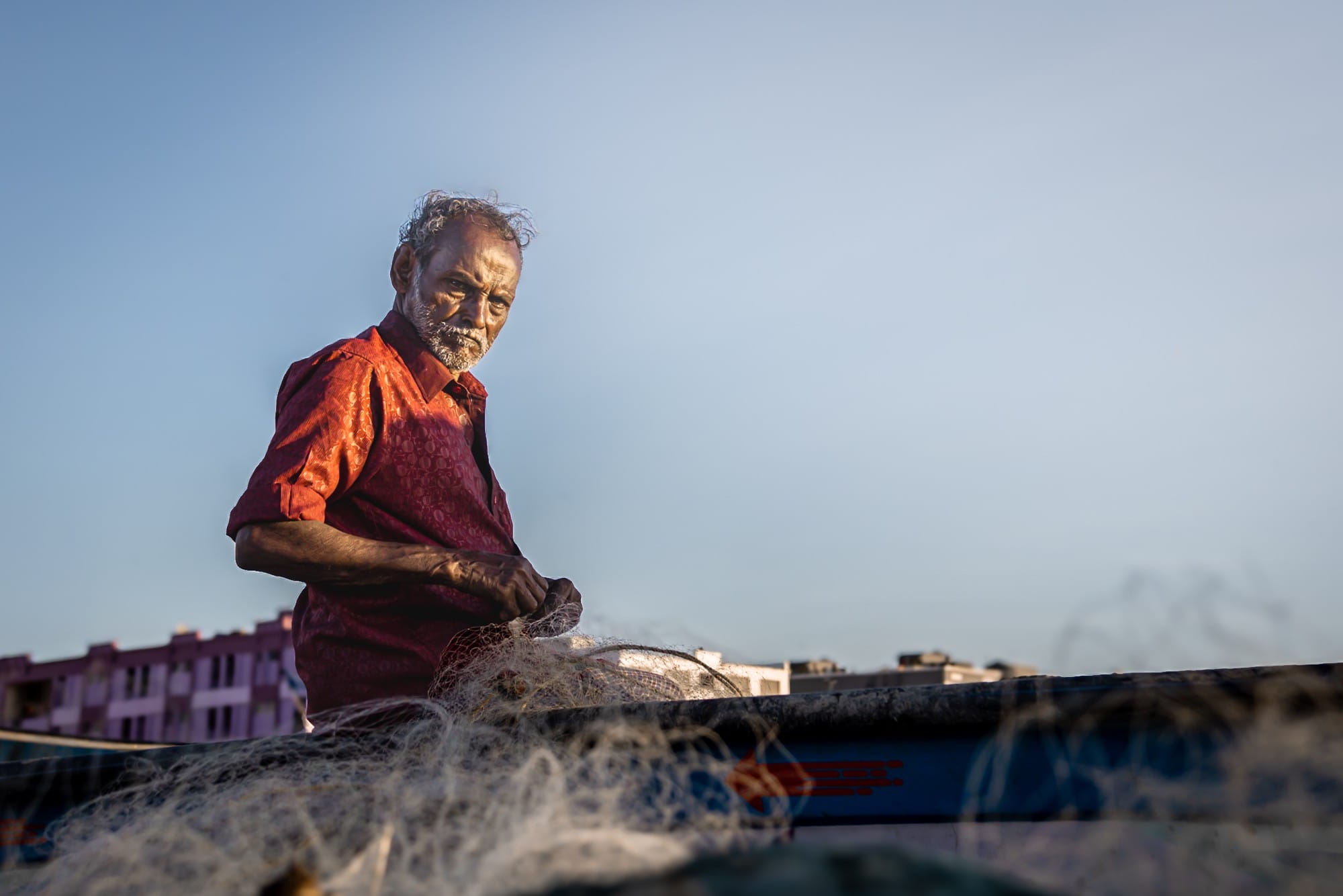 Older fisherman in a red shirt standing beside fishing nets.