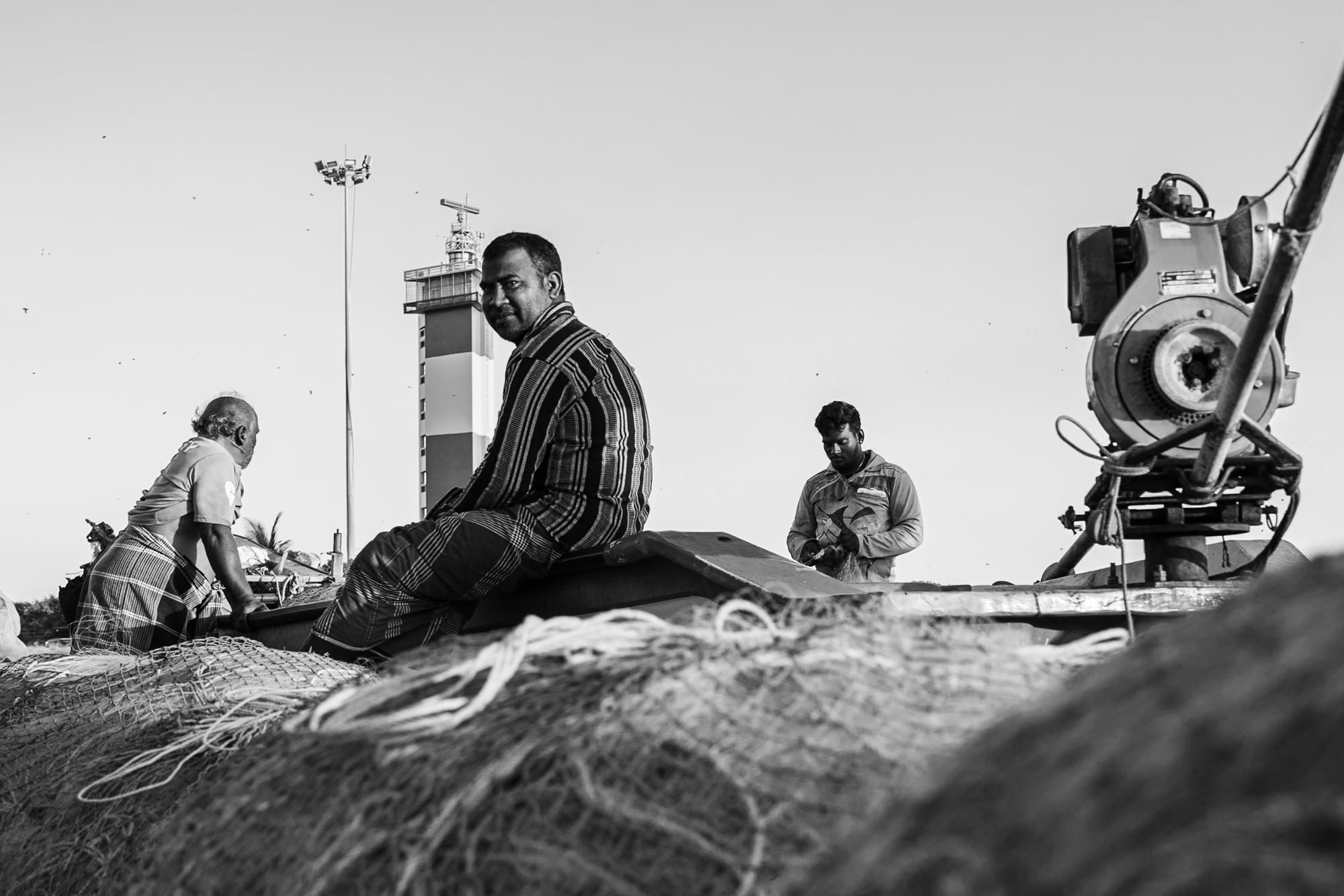 Black-and-white photograph of fishermen sitting on a boat surrounded by nets.