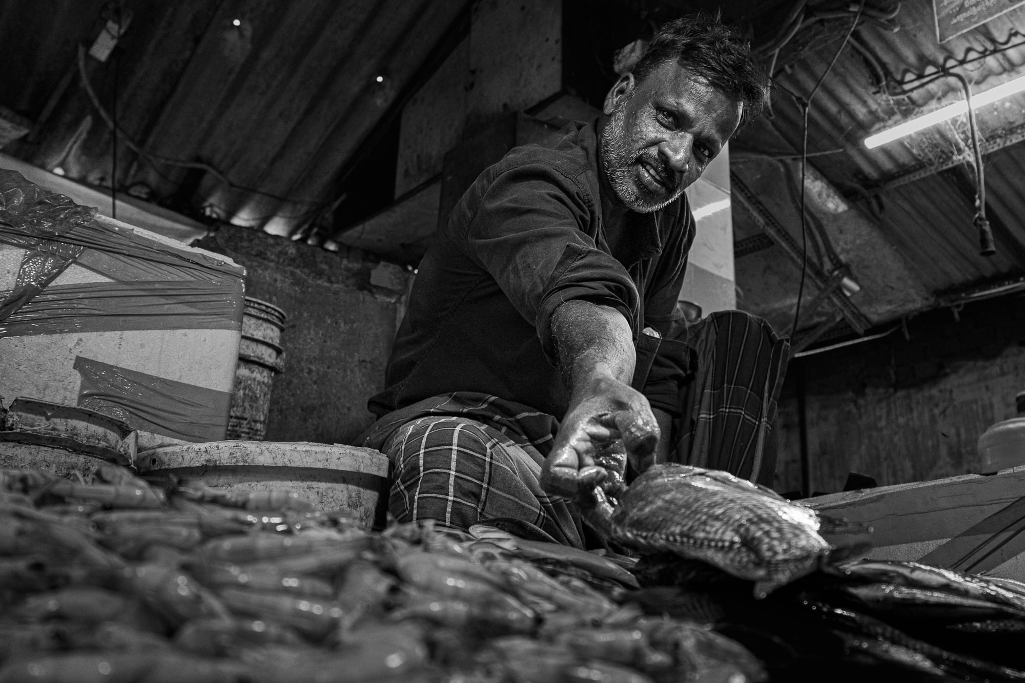 Black-and-white photograph of a vendor leaning forward over a display of fish.