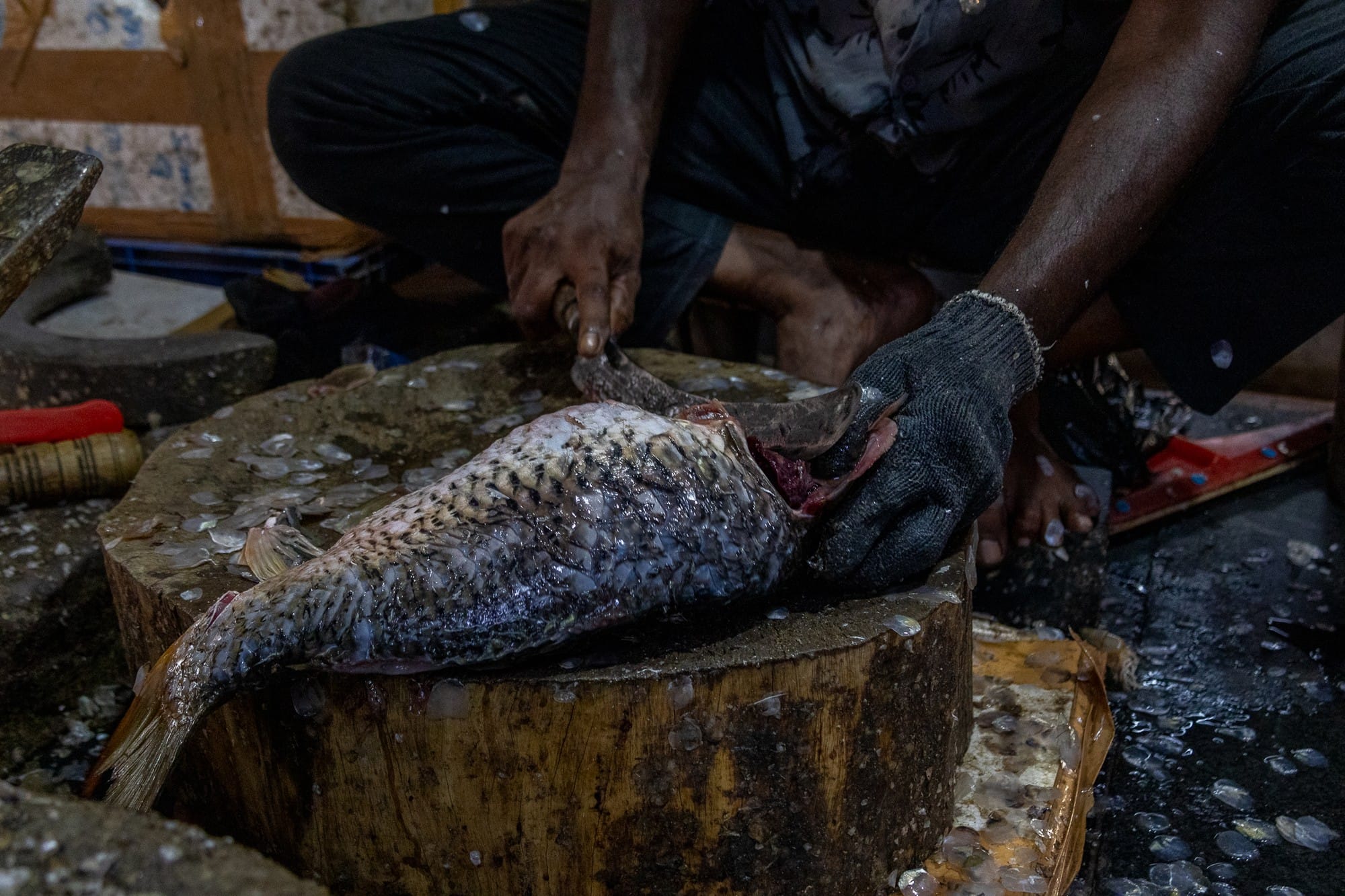 Close-up of a worker preparing a large fish on a wooden cutting block.