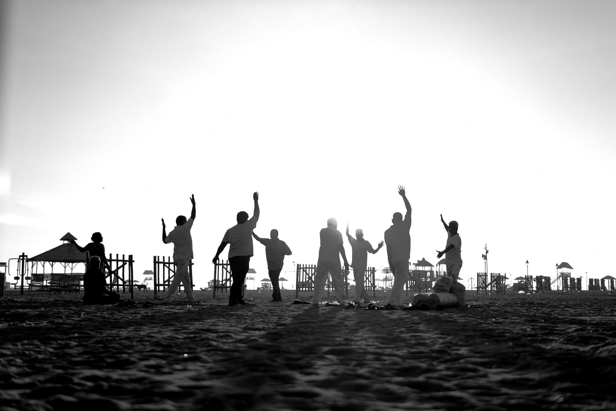 Black-and-white silhouettes of people playing a game on the beach.